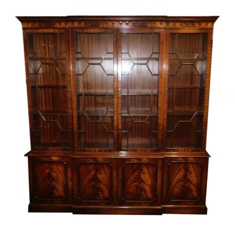 A Reprodux Georgian style mahogany break front bookcase, the outswept pediment with dentil moulding, over four doors enclosing shelves, the lower section with four cupboard doors, raised on a plinth base, with keys, 214cm H, 203cm W, 39.5cm D.