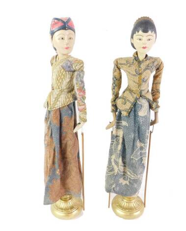 A pair of Indonesian carved wood rod puppets, fully clothed, comprising two women on gilt stands, 58.5cm H.