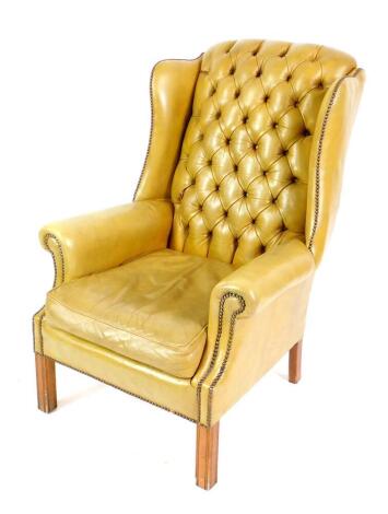 A Georgian style mahogany wingback armchair, with button back tan leather upholstery, loose seat, raised on fluted square legs.