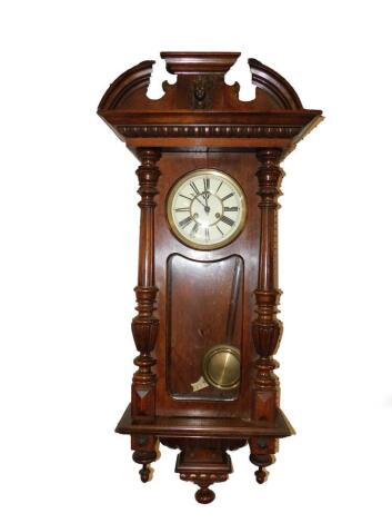 A Continental walnut cased Vienna wall clock, circular enamel dial bearing Roman numerals, eight day movement with coil strike, the case with broken arch pediment above a glass door flanked by turned and fluted pilasters, with key, 121cm H.