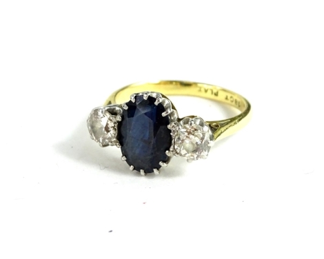 A sapphire and diamond ring, with a central oval cut sapphire flanked two diamonds set in yellow metal stamped 18ct plat. Insurance valuation conducted 19/9/91, for £2700.