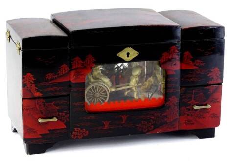 A novelty oriental jewellery box, the hinged lid enclosing a mirror and various compartments above a glass panel enclosing a rickshaw group in simulated ivory, the lacquered case overall decorated with a river landscape in black and deep red on bracket fe