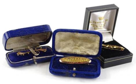 Three gold brooches, to include a 9ct gold Victorian "mother" brooch, stamped to back JC, 4cm W, in fitted case, a 9ct gold curved design bar brooch, with central seed pearl set design, 4cm W, in fitted box and a 9ct gold S Brothers Victorian heart and le