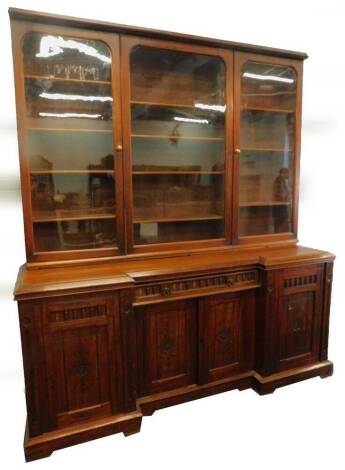 A late Victorian walnut bookcase, the top with three glaze doors, enclosing adjustable shelves, the inverted breakfront base with a central frieze drawer flanked by two panel doors, each with split turning decoration and Gothic style brass handles, on a p