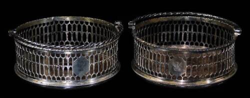 A pair of George III silver coasters, of circular form, each with a pierced body and swing handle, with crest, on circular wooden feet, London probably 1769, 12cm W. (2)