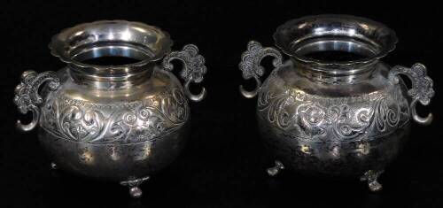 A pair of Chilean vases, each of squat circular form, with floral rims and shaped S scroll handles, each body decorated with a banding of flowers, on triple hoof feet, marked O900 Chile, white metal, 9cm H, 12oz. (2)