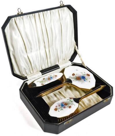 A cased enamel dressing table set, comprising hairbrush, 24cm W, clothes brush and hand mirror, each with a floral enamel on base metal ground. (cased)