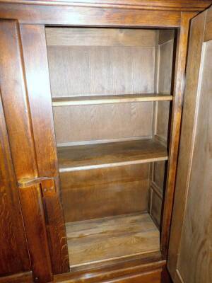 An oak Arts & Crafts style cupboard, with plain fixed cornice raised above two panel doors revealing fitted interior above two drawers beneath, on scroll feet, 183cm H, 155cm W, 50cm D. - 2