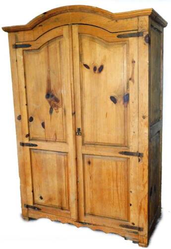 A rustic pine cupboard, the arched top above a pair of panelled doors with heavy metal hinges, revealing a shelf above two drawers, raised on stiles, 193cm H, 137cm W, 67cm D.