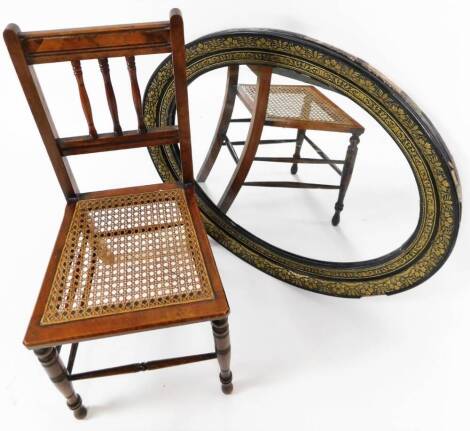 A 19thC oval mirror, partially ebonised and raised with various leaves, in gilt colours with plain glass, 80cm H, 90cm W, 5cm D and a bergere salon chair. (2)