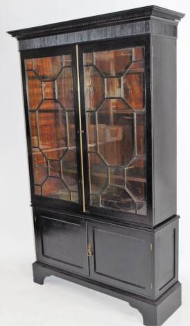 An ebonised bookcase, with dentil and line cornice raised above a pair of astragal glazed doors, with double cupboard beneath, on front bracket feet, 178cm H, 115cm W, 39cm D.