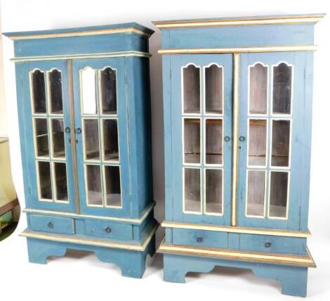 A pair of painted floor standing cabinets, each in turquoise and cream, with a shaped cornice, arched glazed doors and ring handles with plain escutcheons, above two short drawers, on elaborate stylized bracket feet, 172cm H, 99cm W, 36cm D. (2)