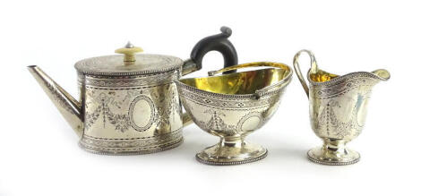 A Victorian silver three piece bachelor's tea set, the oval teapot with ivory knop and ebonised handle, engraved overall with leaves, scrolls, etc., matching milk jug and a sugar bowl with loop handle, each with piece with an oval vacant cartouche, London