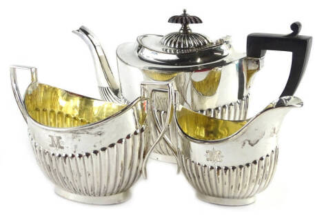 An Edwardian silver three piece tea set, each with part fluted decoration, the teapot with ebonised knop and handle, comprising a teapot, two handled sugar bowl and milk jug, engraved with the letter M, Sheffield 1903, 25oz gross.