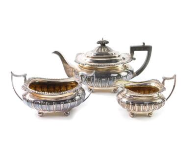 A George V silver semi fluted three piece tea set, the rims with gadrooned and embossed shell decoration, raised on four ball feet, comprising tea pot, cream jug and sugar bowl, Sheffield 1916, 45.05oz.