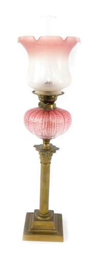 An early 20thC brass Corinthian column oil lamp, with a fluted cranberry glass reservoir, with chimney, and floral etched clear to cranberry glass frilled shade, 79cm H.