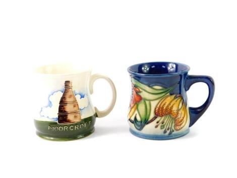 A Moorcroft pottery mug, decorated in the Bottle Kiln pattern, and a further mug decorated in the Anna Lily pattern, impressed and painted marks. (2)