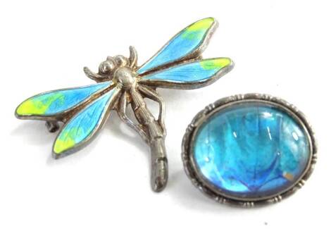 Two modern silver brooches, to include a silver and enamel dragonfly brooch, the wings with blue and green enamel design, lacking pin back, 3cm W, an d a silver and butterfly wing circular brooch, makers stamp to rear SW and Co, 2cm W. (2)