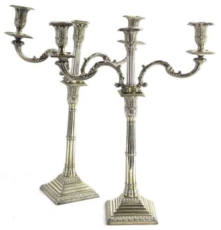 A pair of silver plated three branch candelabra, each with a cluster column, headed by a leafy capital on a square stepped base, 49cm H, 39cm W.