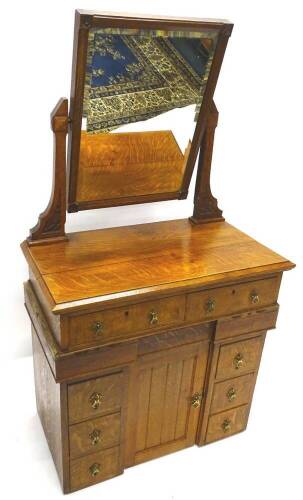 A late Victorian oak Gothic dressing table, the raised back with a rectangular bevelled plate, above two frieze drawers, the base with an arrangement of four short drawers around a panelled door, on an inverted breakfront plinth, 79cm W.