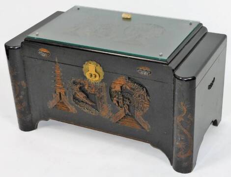 A 20thC Chinese lacquer camphor wood chest, of shaped rectangular form, the glass top revealing a heavily carved panel section of buildings, figures and boats, with a heavily carved front and lock, c1957, with key and receipt of sale, 50cm H, 93cm W, 52cm