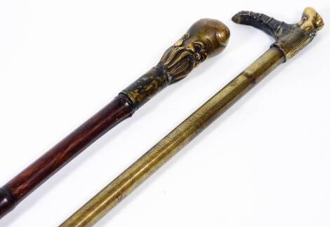 A Chinese bamboo type walking stick, with rubber end and metal top, set with a figure of a bearded sage, 92cm H, and a further walking stick with a repeat geometric and letter stem, rubber end and shaped handle. (2)