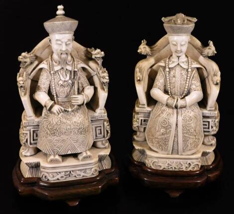 A pair of finely carved 19thC Chinese ivory figures, of a lady and gentleman, each in Imperial dress seated in thrones on shaped bases, expertly carved and each wearing bead necklaces, on wooden plinth bases, 21cm H. (2)