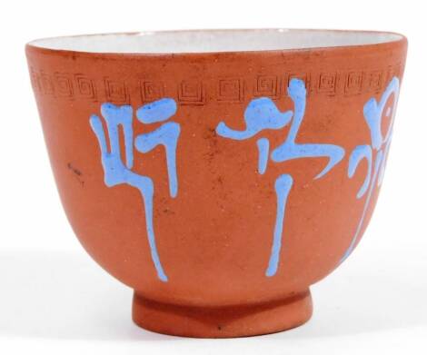 A Chinese red ware pottery tea bowl, the bell shaped body, with an upper Greek key style design, handpainted with blue on red ground, on a circular foot, unmarked, 8cm Dia.