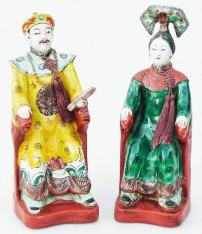 Two early 20thC pottery figures, of seated figures in flowing robes, polychrome decorated predominately in yellow, green and brown, unmarked, 25cm H. (2, AF)