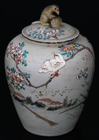 A Japanese late Meiji period jar and cover, with rat knop, polychrome decorated with birds, buildings and flowers, predominately in green, pink and white, impressed mark beneath, 14cm H.