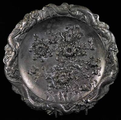 A 20thC Japanese white coloured metal plate, of shaped circular form with a dragon border and repoussé decorated with flowers to the centre, unmarked, 33cm W and a base metal tray. (2) - 2