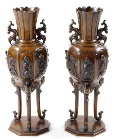 A pair of Japanese patinated bronze vases, each with floral stems flanked by S scroll handles, each shaped body raised with panels of figures, on three scroll legs terminating in hexagonal platforms, unmarked probably Meiji period, 26cm H.