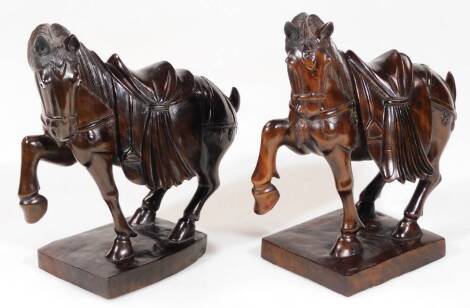 Two hardwood Chinese horses, in the Tang style, each with front legs raised on square bases, heavily carved, 23cm H. (2)