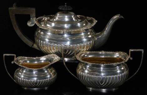 A George V silver three piece tea service, comprising teapot of cape form, two handled sugar bowl and milk jug, each partially gadrooned with an upper floral banding and partial silver gilt interior on oval feet, Birmingham 1915, the teapot 15cm H, 34oz a