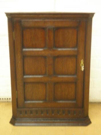 A small oak hanging corner cabinet with a single panel door<br