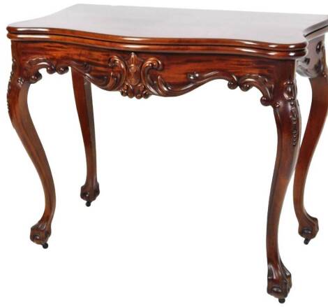 A George III style mahogany serpentine card table, the baize lined fold over top raised above a heavily carved frieze, on inverted cabriole ball and claw feet with further carved scrolls to each side, when closed 76cm H, 91cm W, 49cm D.