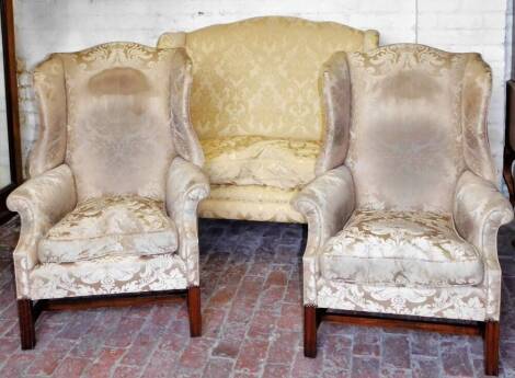 A matched 19thC three piece lounge suite, comprising two seater settee and two chairs, each wing back with elaborate floral decoration in gilt and white, the settee on turned front legs, the wing chairs on square block legs joined by H stretchers, 118cm H