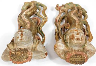 A pair of heavily carved Javanese wooden serpent child nymphs or mermen, each looking upwards on similar pierced bases, partially painted, 33cm W. - 2