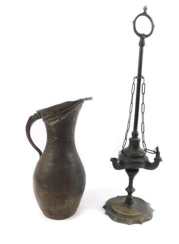 A 19thC brass oil lamp, of Roman oil lamp form, with long carrying handle, the body with three apertures, raised on a serpentine circular base, 48cm H, together with a Middle Eastern metal ewer, engraved with panels of birds, floral emblems and foliate sc