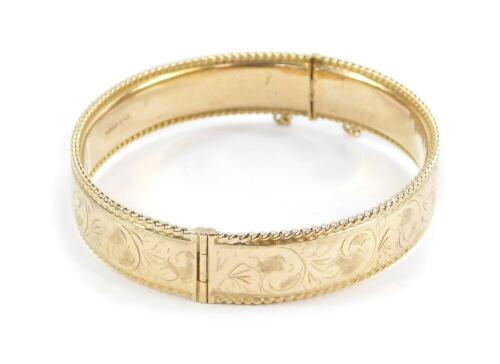 A 9ct gold bangle, with engraved foliate decoration, on a snap clasp with safety chain as fitted, 20.3g.