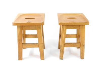 A pair of late 20thC oak stools, with saddle seats, raised on tapering square legs united by stretchers.