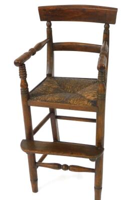 A Regency faux rosewood child's highchair, with a bar back, turned arms, rush seat, raised on turned legs united by stretchers, with a footrest, metal guardrail lacking.