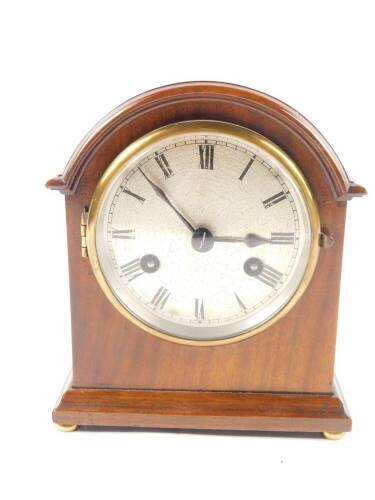 An early 20thC mahogany cased mantel clock, circular silvered dial bearing Roman numerals, Continental eight day movement with coil strike, the case of domed form, raised on a stepped base, with brass feet, with key, 20cm H, 17cm W, 11.5cm D.