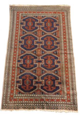A Persian silk rug, decorated with eight guls, against a blue ground, within a red and grey repeating floral border, 210cm x 122cm.