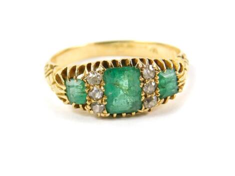 An 18ct gold emerald and diamond three stone ring, set with three cushion shaped emeralds, interspersed with three brilliant cut diamonds at two intervals, size L, 4.0g.