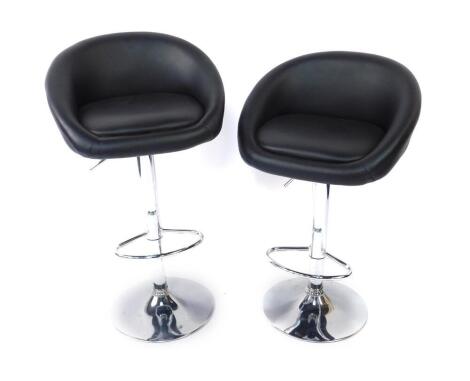 A pair of white metal and black leather tub bar stools, with foot rests, raised on a circular base.