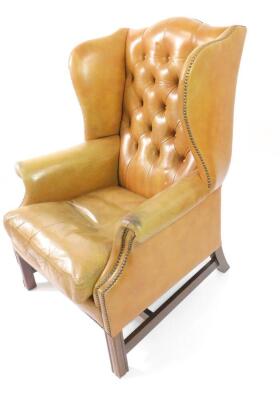 A Georgian style mahogany wing back club armchair, upholstered in button back tan leather, with loose cushion raised on fluted square legs united by an H-frame stretcher, 106cm H. - 2