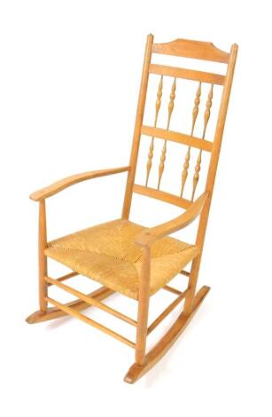 A Neville Neal ash rocking chair, after a design by Ernest Gimson, with a spindle turned back and rush seat, stamped Neville Neal to upright.