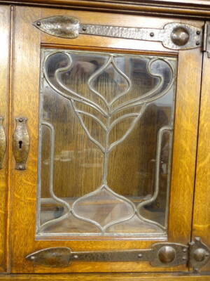 A late 19thC oak Arts and Crafts sideboard in the manner of Liberty, the raised back with two leaded glazed doors, each with hammered copper hinges and fittings, the bow fronted base with two drawers above two doors, with similar hammered fittings, on blo - 2