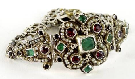 An Eastern style bracelet, set with various paste stones, of green and red colour, and seed pearls on white metal, unmarked, boxed.